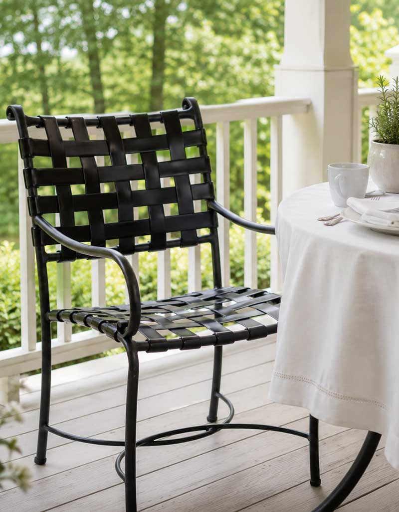 Black strap dining chair with a woven seat on a porch beside a table with a white cloth
