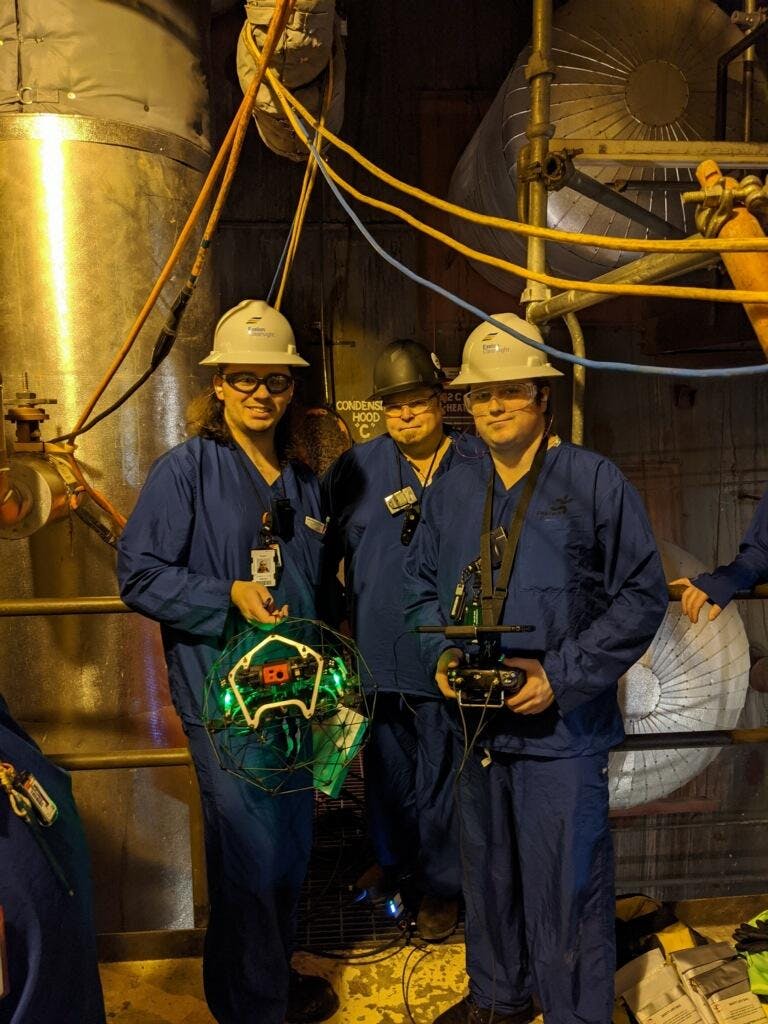 Three men in hardhats, blue suits, and safety goggles