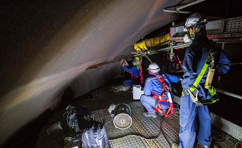 A team of inspection experts work together in a confined space wearing protective helmets and gear in industrial facility.