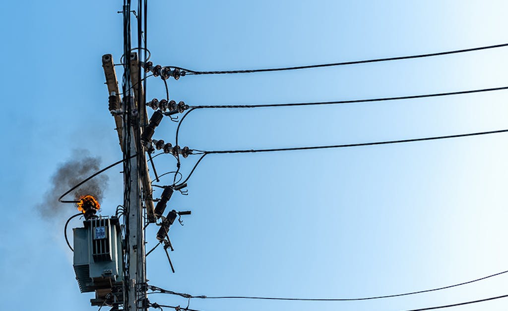Power pylon overload or electric short circuit at transformer on poles and fire or flame with smoke on blue sky.
