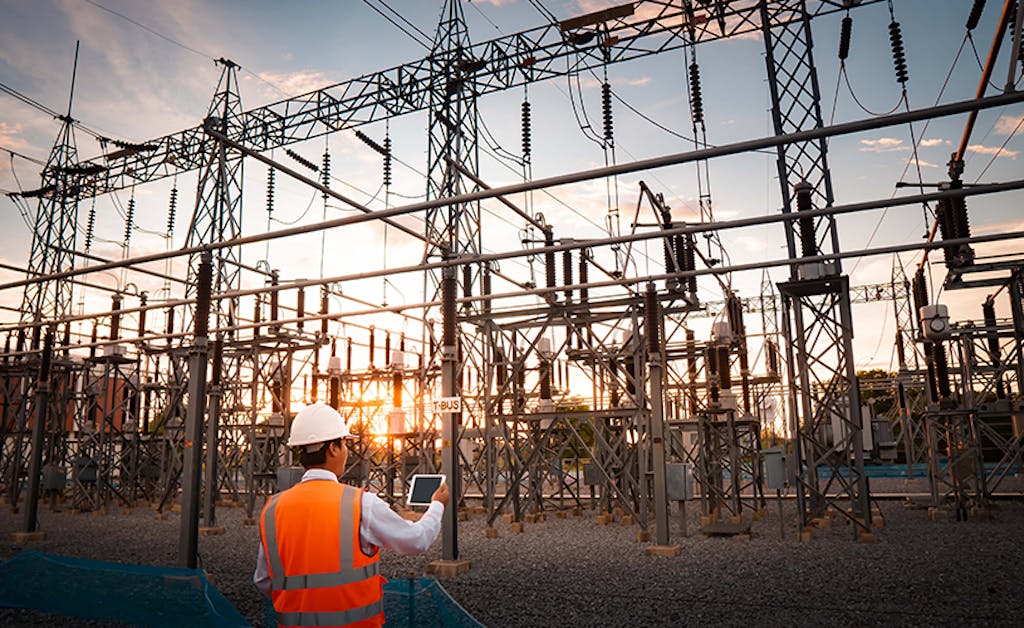 Electrical inspector analyzes data collected on a screen in his hand while onlooking an electrical substation.