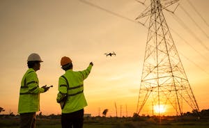 Two electrical engineers using drones to inspect electrical towers at sunset.