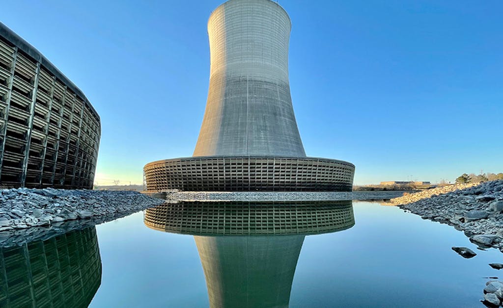 The outside of a cooling tower with blue sky background and water reflecting the tower in front.