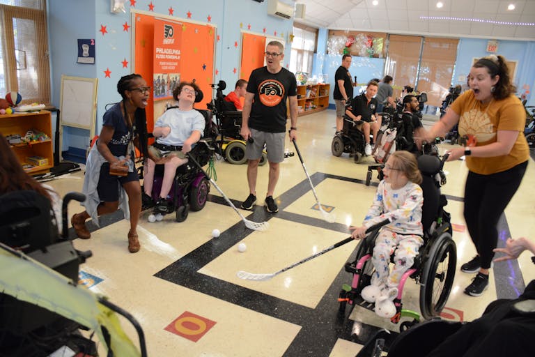 Students in powerchairs play with adapted hockey sticks, celebrate a goal.