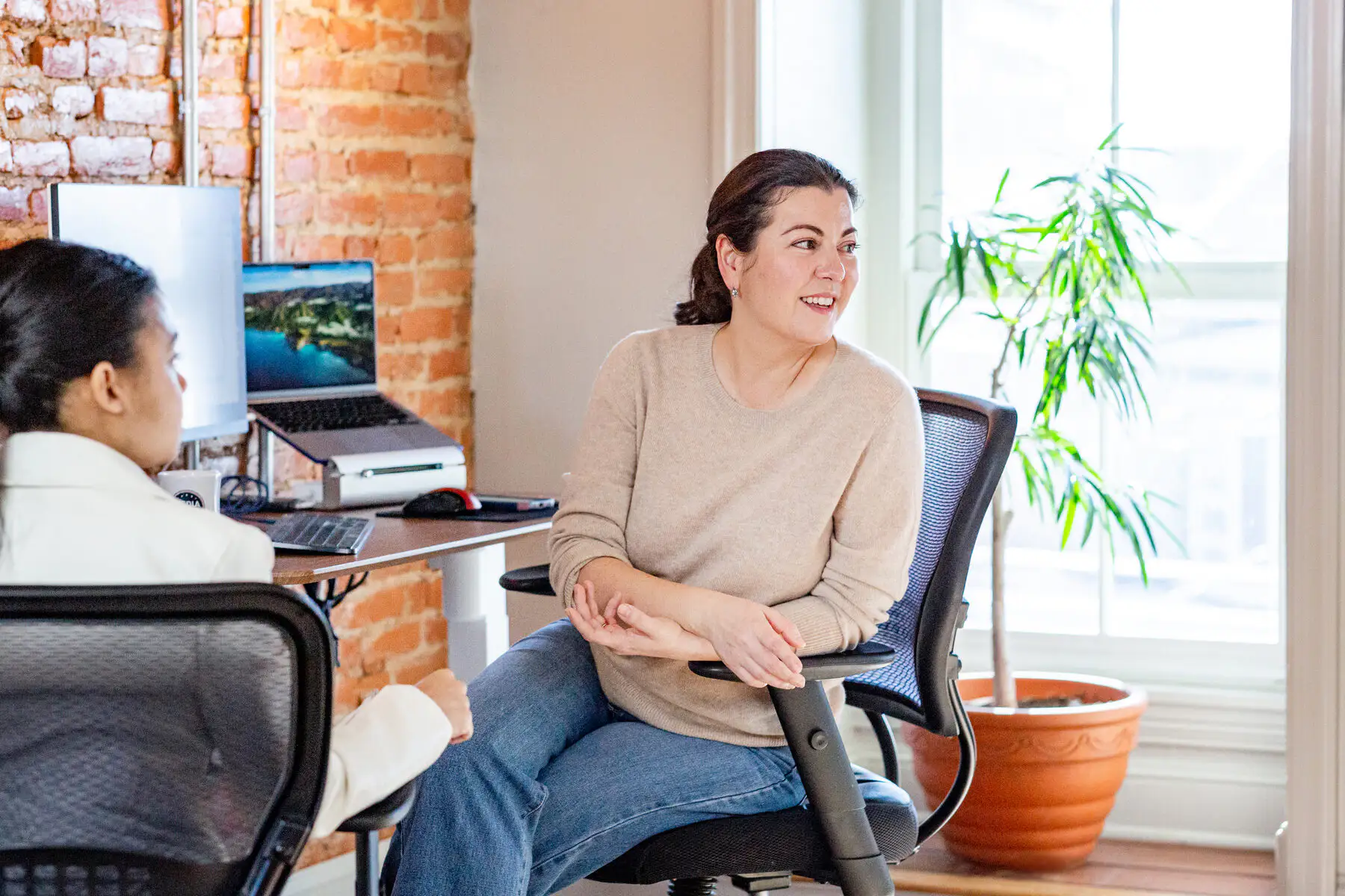 Two Media Proper team members talking at a desk by the studio’s brick wall