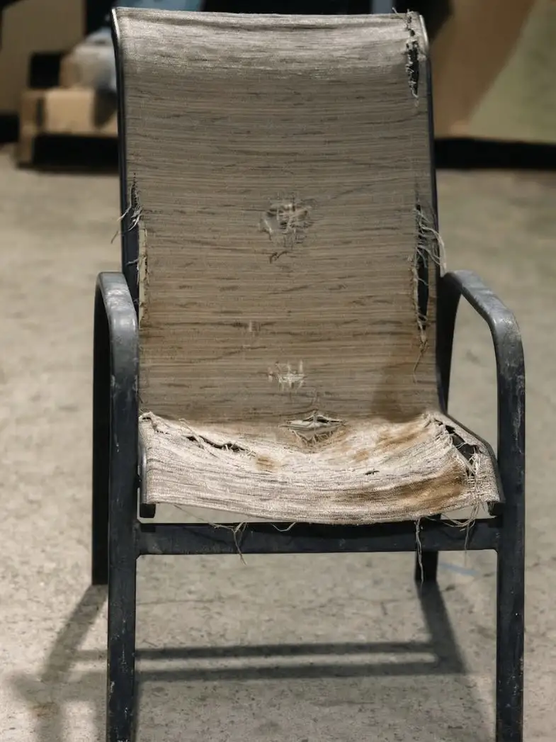 A patio chair with its sling fabric shredded and hanging loose