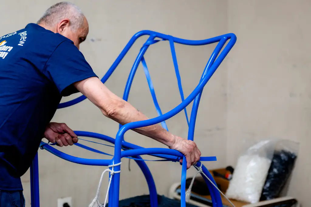 A technician restrapping a freshly powder-coated blue chair frame in the Willow Grove workshop