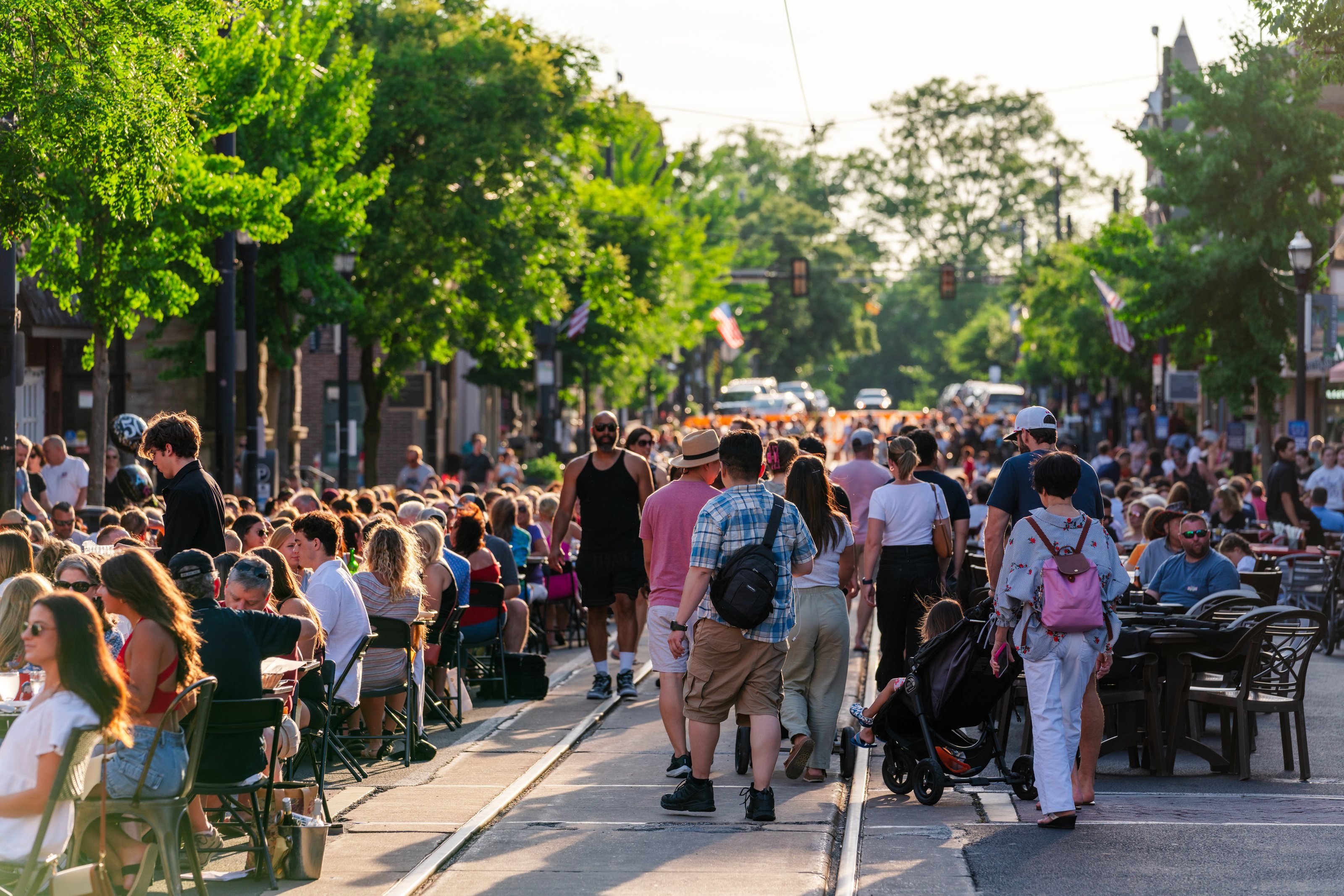 Dining Under the Stars at golden hour: diners at tables down both sides of State Street while people walk the middle of the street over the trolley tracks