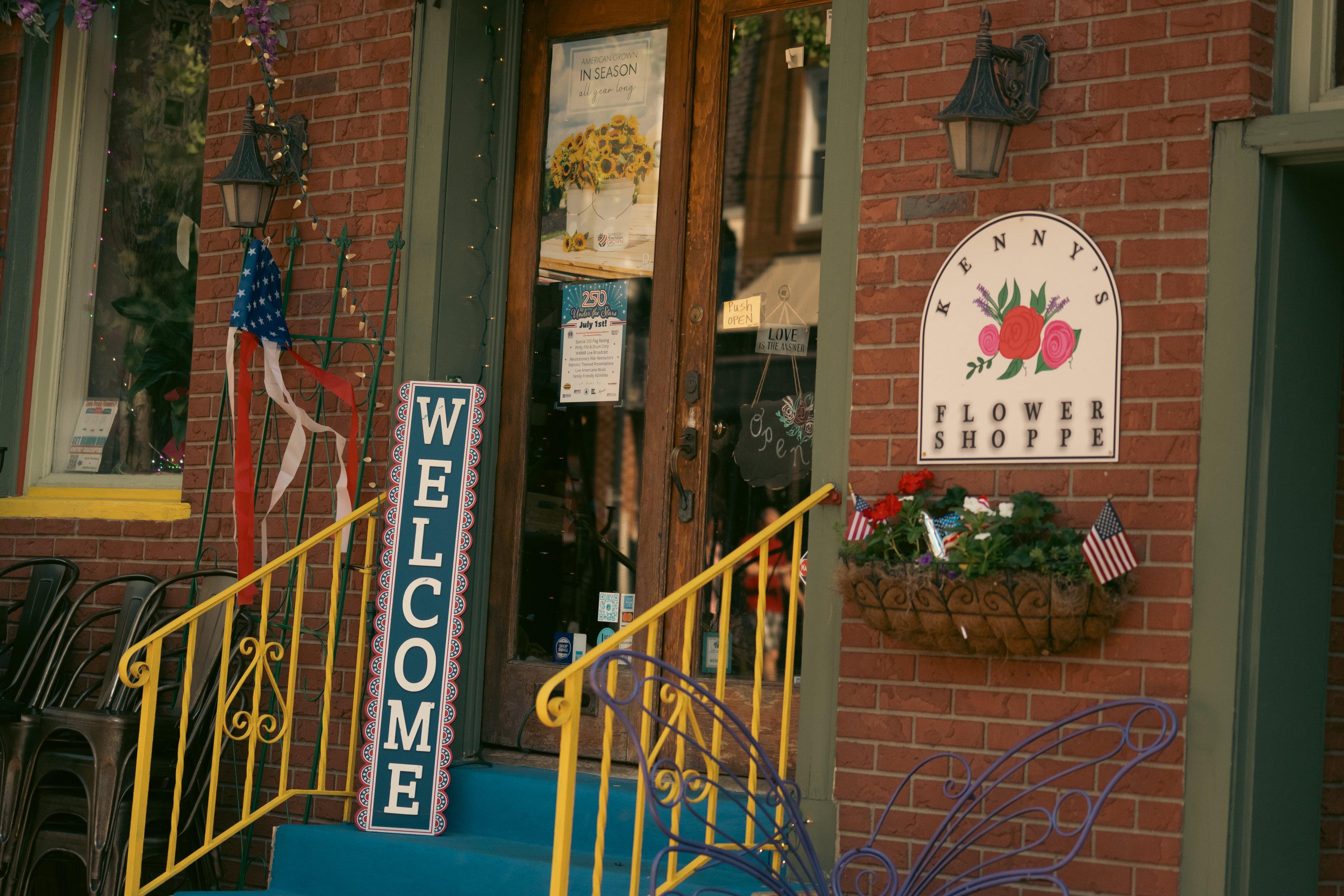 Brick storefront on State Street with a yellow iron railing, a WELCOME sign and a flower shop sign