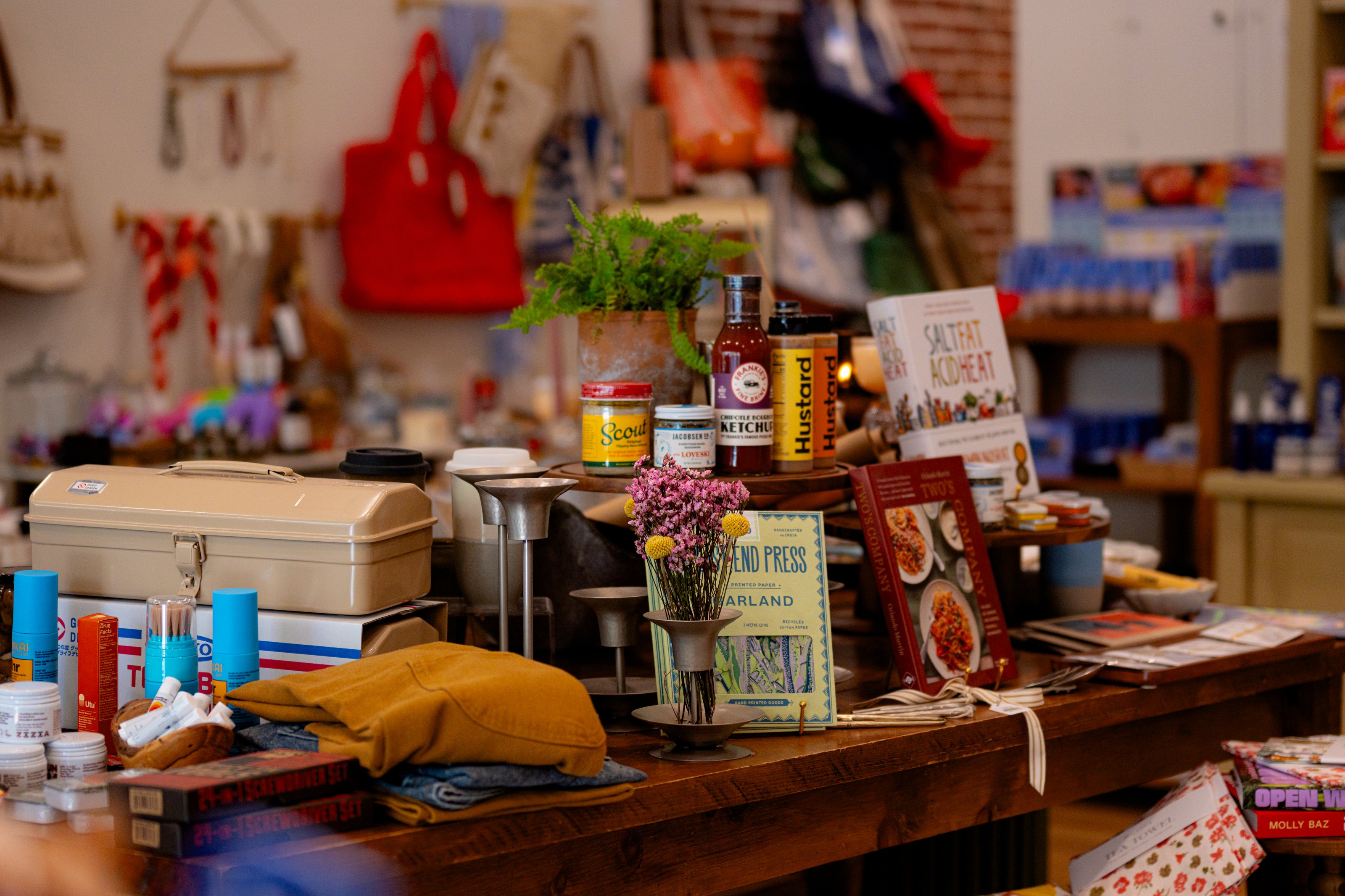 A boutique table in a Media shop: red leather bag, candles, books and local goods on warm wood